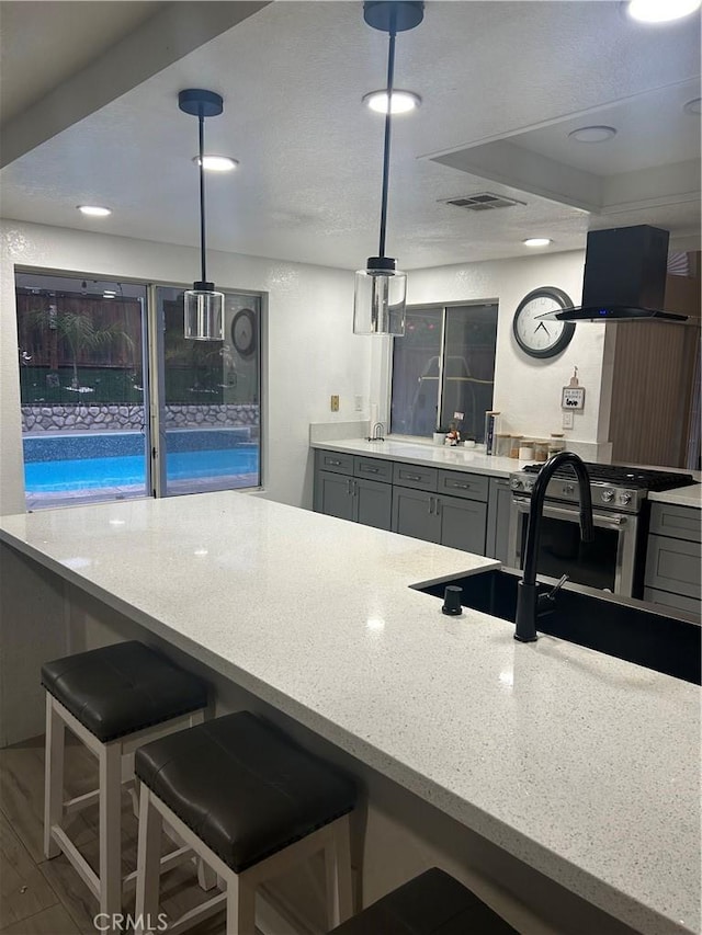 10075 Desert Mallow, Moreno Valley, CA 92557 - kitchen with exhaust hood, a kitchen breakfast bar, stainless steel gas stove, visible vents, and gray cabinetry