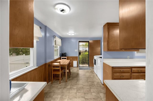 kitchen with wainscoting, brown cabinetry, washing machine and clothes dryer, light countertops, and wood walls