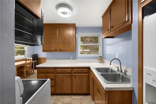 kitchen featuring brown cabinetry, a sink, stove, and light countertops