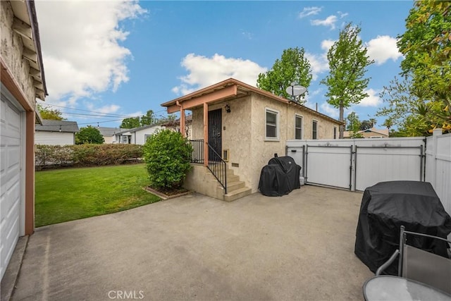 rear view of property featuring stucco siding, a gate, fence, a patio, and a lawn