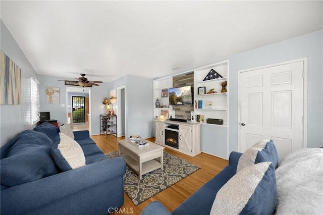 living room featuring a lit fireplace, a ceiling fan, and light wood-style floors