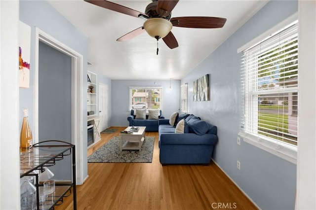 living area with wood finished floors, a ceiling fan, and a glass covered fireplace
