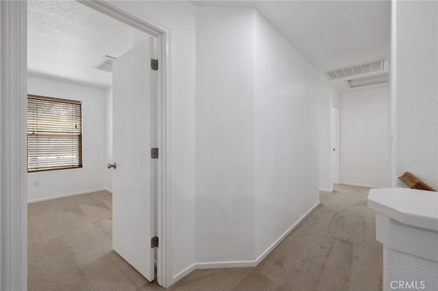 hallway featuring baseboards, visible vents, and light colored carpet