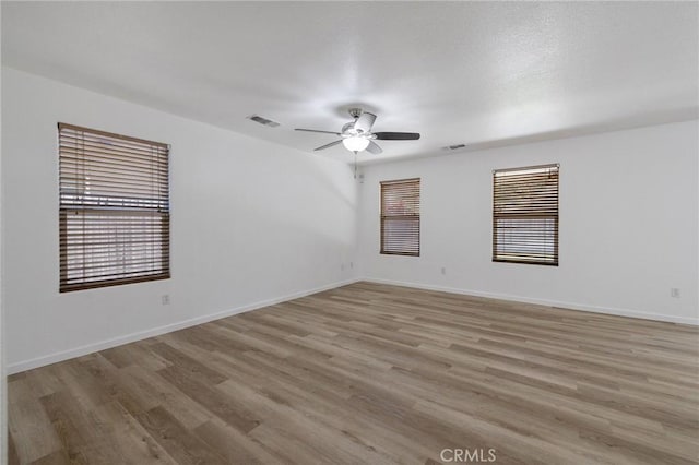 spare room with light wood-type flooring, visible vents, a ceiling fan, and a healthy amount of sunlight