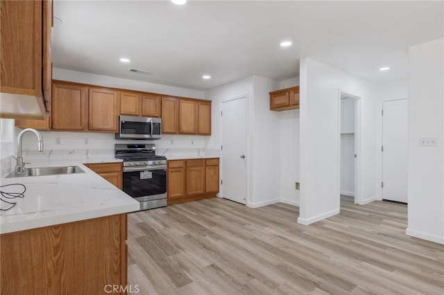 kitchen featuring visible vents, appliances with stainless steel finishes, brown cabinets, a sink, and light wood-type flooring