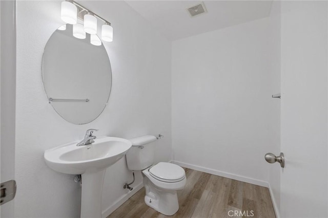 bathroom with toilet, visible vents, wood finished floors, and baseboards