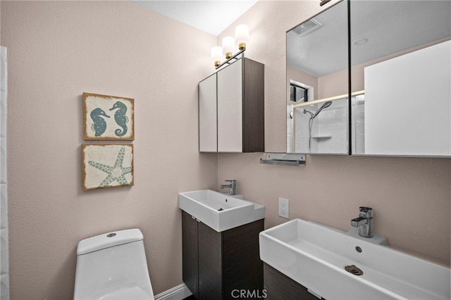 bathroom featuring two sinks, toilet, visible vents, and walk in shower