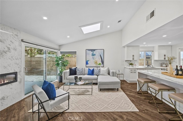 living area featuring visible vents, a wealth of natural light, vaulted ceiling with skylight, and dark wood-type flooring