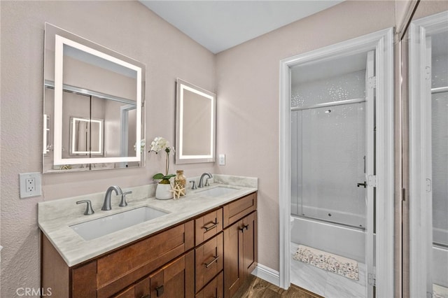 bathroom with shower / bath combination with glass door, wood finished floors, double vanity, and a sink