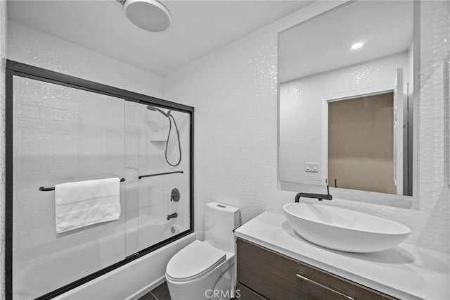 full bathroom with toilet, combined bath / shower with glass door, a textured wall, and vanity