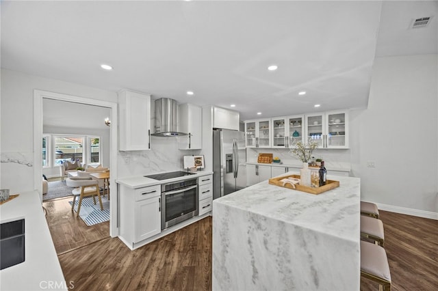 kitchen with a kitchen island, wall chimney exhaust hood, appliances with stainless steel finishes, and dark wood-type flooring