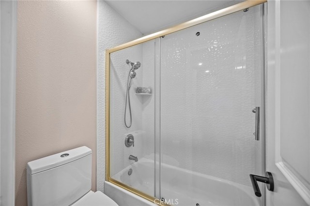 full bathroom featuring bath / shower combo with glass door, toilet, and a textured wall