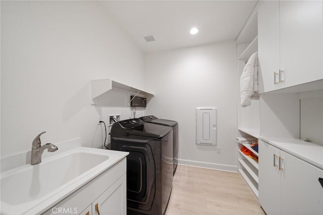 laundry area featuring cabinet space, a sink, separate washer and dryer, light wood-style flooring, and baseboards