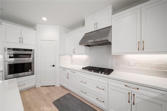 kitchen featuring light wood-type flooring, light countertops, white cabinetry, under cabinet range hood, and appliances with stainless steel finishes