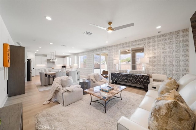 living area featuring visible vents, an accent wall, ceiling fan, wallpapered walls, and light wood-type flooring