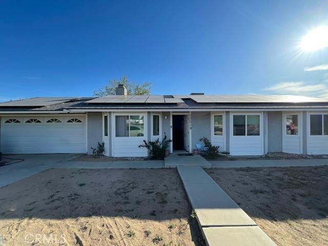 single story home with stucco siding, solar panels, concrete driveway, and an attached garage