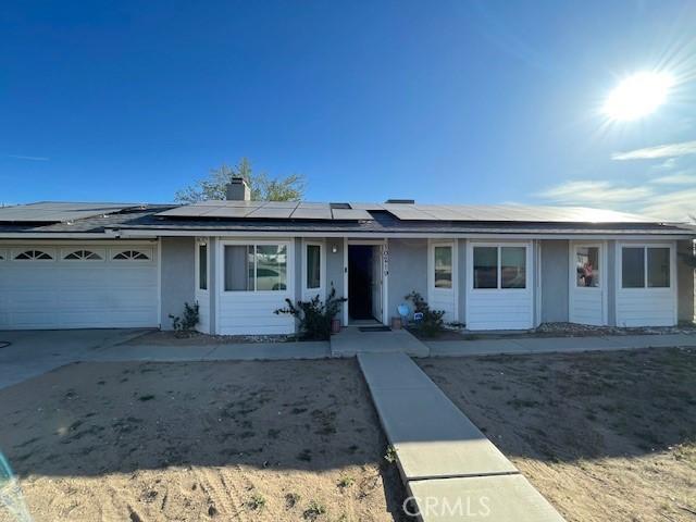 single story home with driveway, stucco siding, solar panels, and a garage