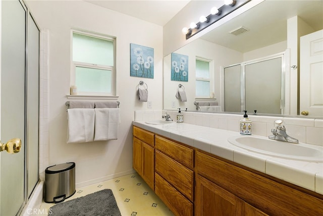 bathroom with visible vents, a shower with shower door, plenty of natural light, and a sink