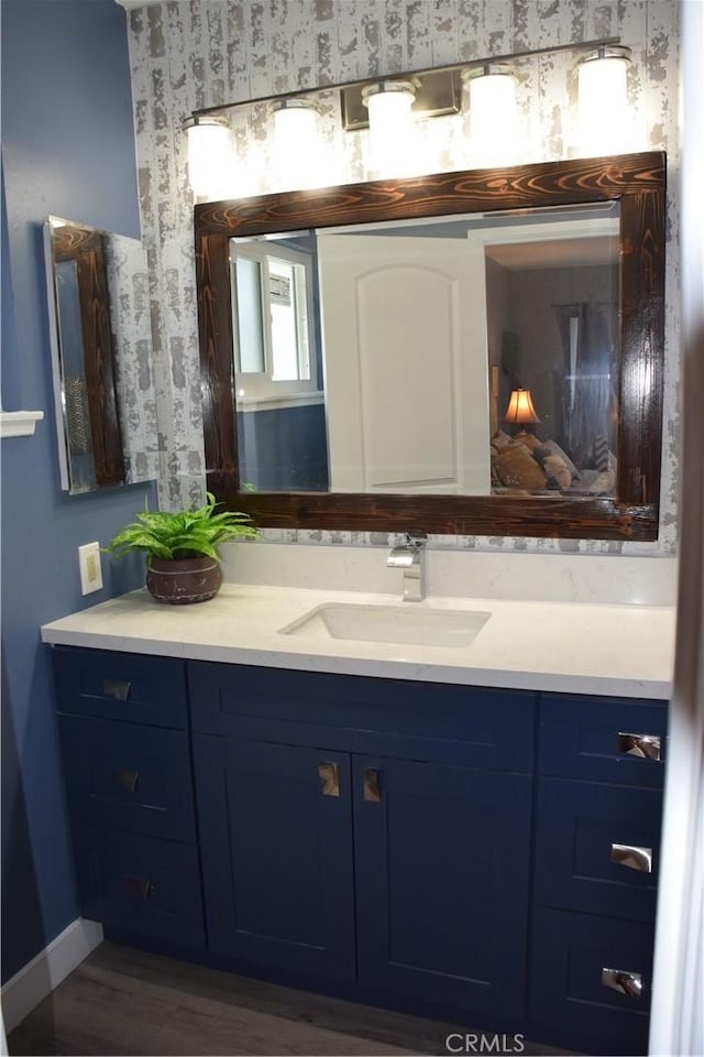 bathroom with wood finished floors, vanity, wallpapered walls, and baseboards