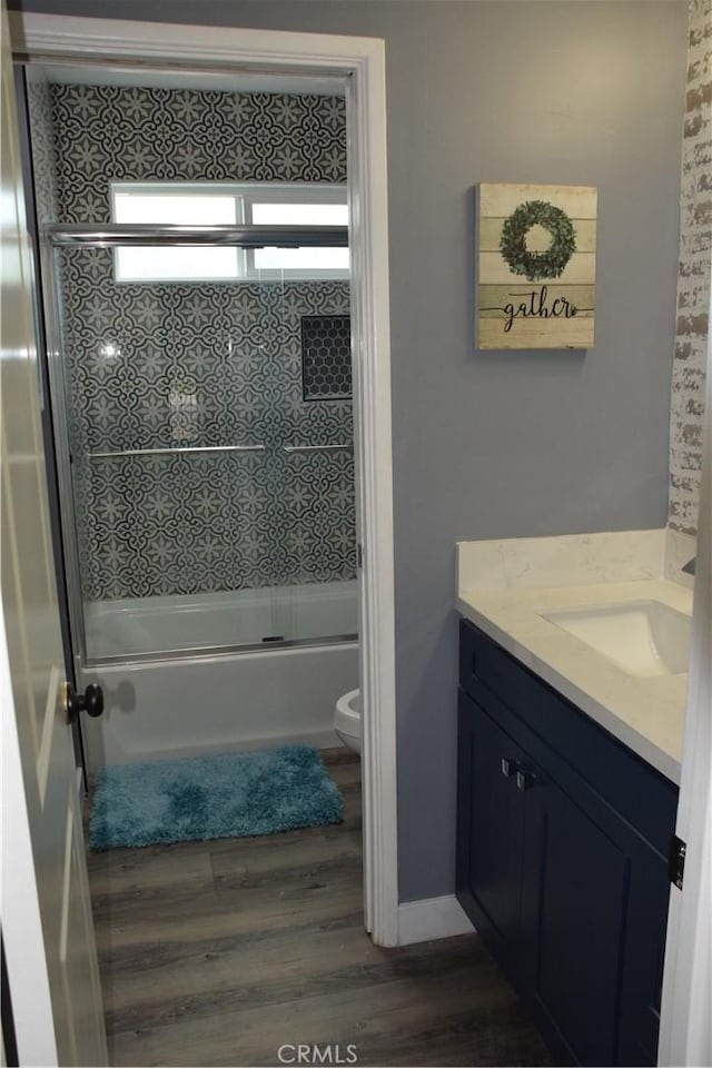bathroom featuring wood finished floors, bath / shower combo with glass door, toilet, and vanity