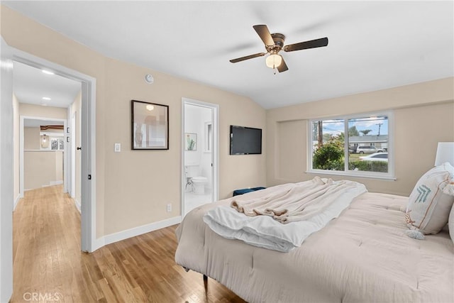 bedroom featuring lofted ceiling, baseboards, light wood-type flooring, a ceiling fan, and ensuite bath