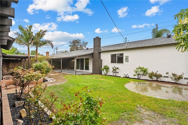 rear view of property featuring a chimney, stucco siding, a yard, a shingled roof, and a patio