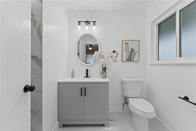 bathroom with baseboards, toilet, vanity, and marble finish floor