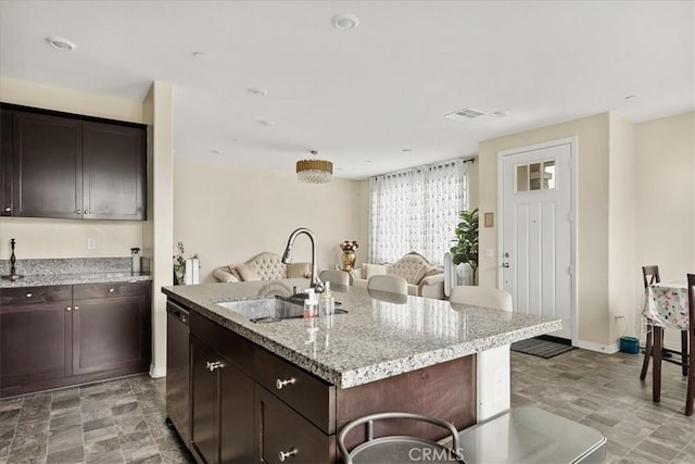 kitchen featuring a kitchen island with sink, a sink, dark brown cabinetry, visible vents, and open floor plan