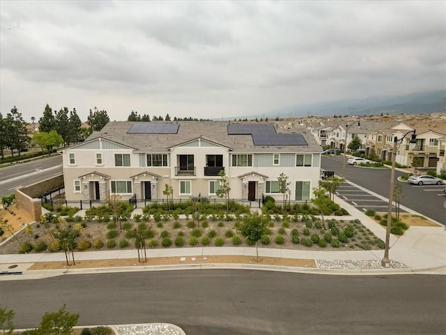 view of front of property featuring a residential view, solar panels, fence private yard, and stucco siding