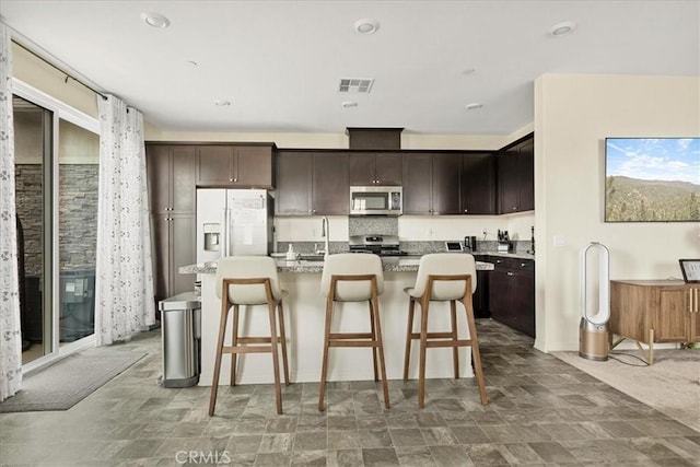 kitchen with visible vents, stainless steel appliances, dark brown cabinetry, a kitchen bar, and an island with sink