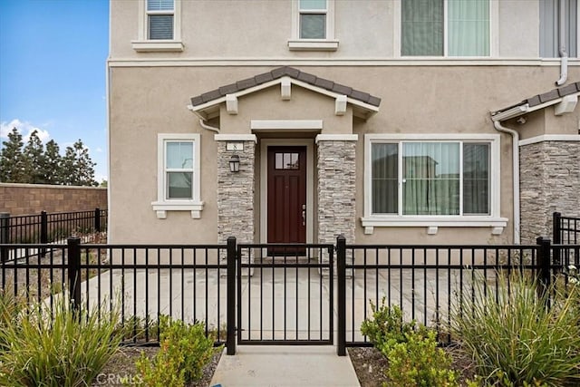 doorway to property with stucco siding, fence, and stone siding