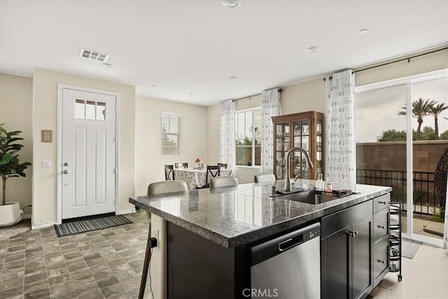 kitchen featuring a sink, a kitchen bar, a center island with sink, baseboards, and stainless steel dishwasher