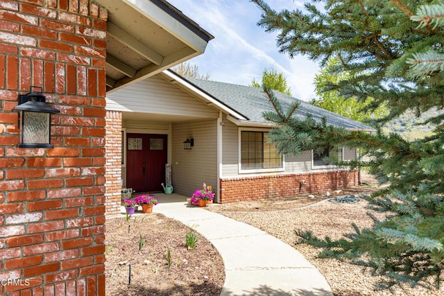 view of exterior entry with brick siding and roof with shingles
