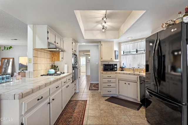 kitchen with decorative backsplash, light tile patterned floors, black appliances, a raised ceiling, and tile countertops
