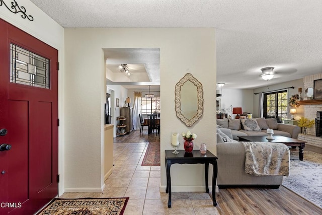 foyer with a textured ceiling, a wealth of natural light, baseboards, and a brick fireplace