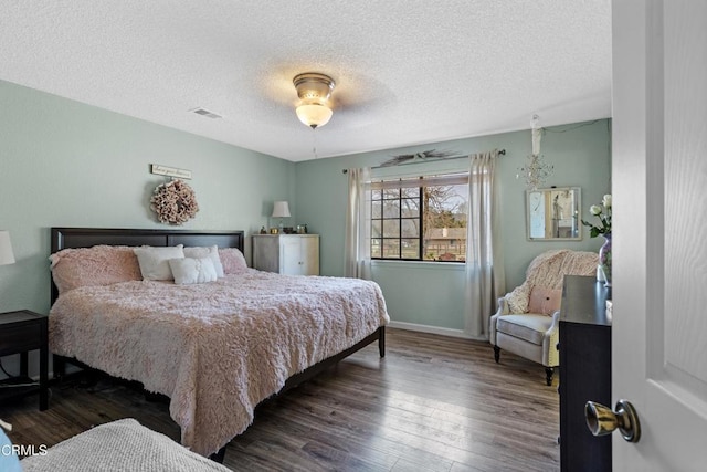 bedroom featuring baseboards, visible vents, wood finished floors, and a textured ceiling