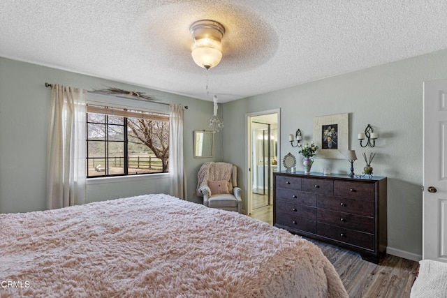 bedroom with a textured ceiling, wood finished floors, ensuite bath, and baseboards