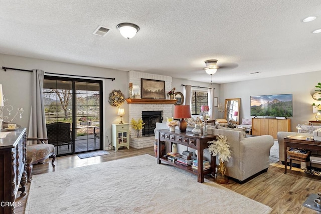 living area with a textured ceiling, visible vents, recessed lighting, a fireplace, and wood finished floors
