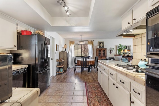 kitchen featuring a raised ceiling, white cabinets, white gas stovetop, and tile countertops