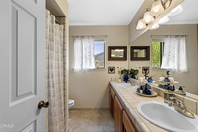 full bathroom with toilet, double vanity, a sink, and tile patterned floors