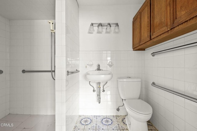 bathroom featuring a sink, toilet, tile walls, tile patterned floors, and tiled shower