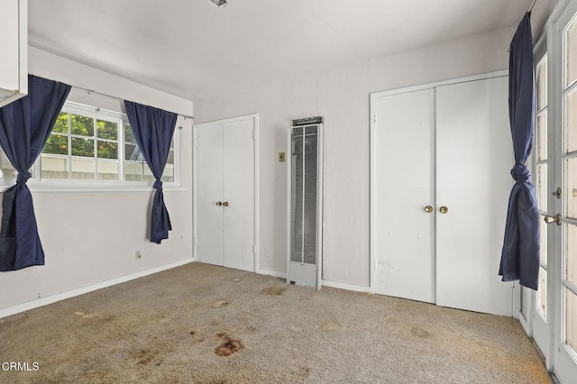 unfurnished bedroom featuring a heating unit, multiple closets, carpet flooring, and baseboards