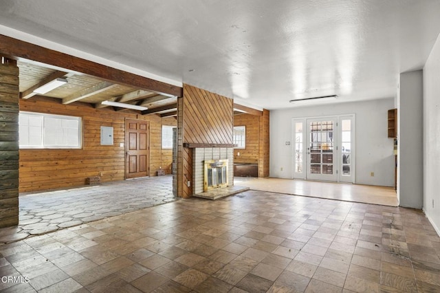 unfurnished living room featuring a large fireplace, electric panel, wood walls, and beam ceiling