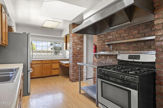 kitchen featuring light wood finished floors, appliances with stainless steel finishes, wall chimney range hood, and light countertops