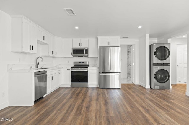 kitchen with stacked washer / drying machine, a sink, stainless steel appliances, baseboards, and light countertops