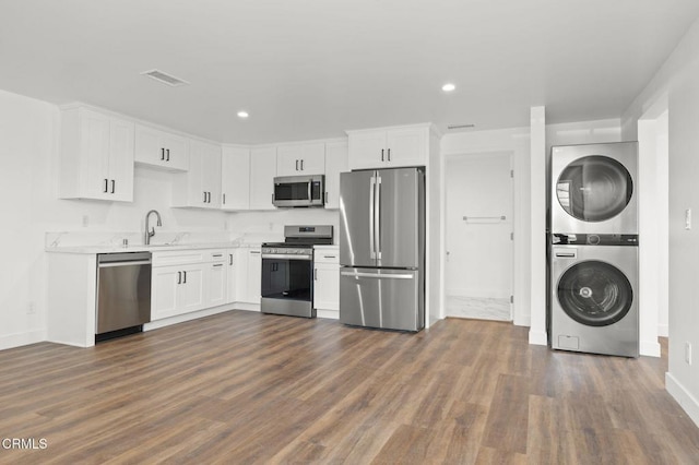 kitchen featuring white cabinetry, stainless steel appliances, stacked washer / drying machine, and a sink