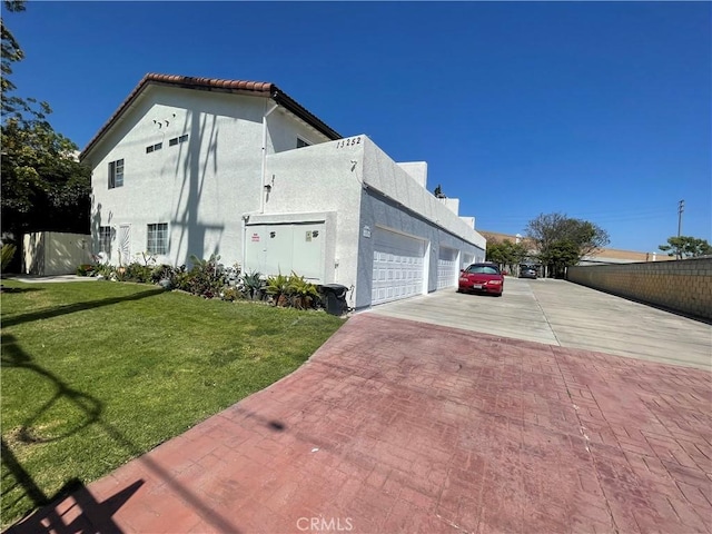 view of property exterior featuring an attached garage, a yard, decorative driveway, and stucco siding