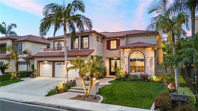 mediterranean / spanish house featuring a garage, a balcony, driveway, stucco siding, and a yard