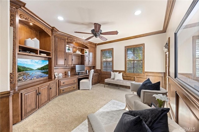 living room with crown molding, wainscoting, built in study area, ceiling fan, and light colored carpet