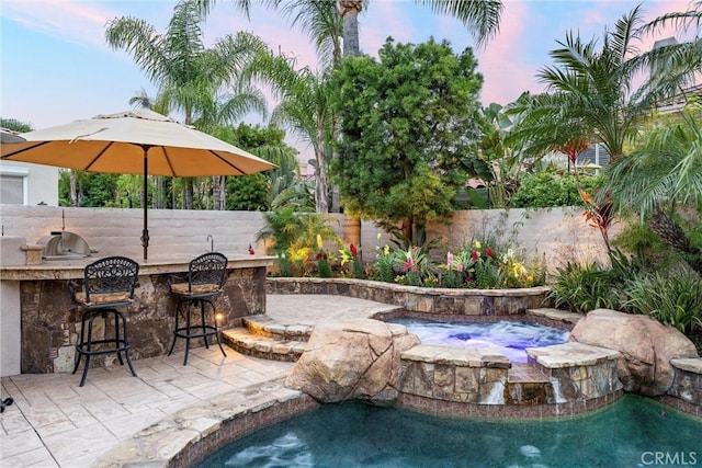 pool at dusk with an in ground hot tub, fence, outdoor dry bar, and a fenced in pool